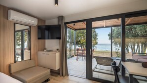 A modern room with a sofa, a dining table, a TV, and a view of the sea.