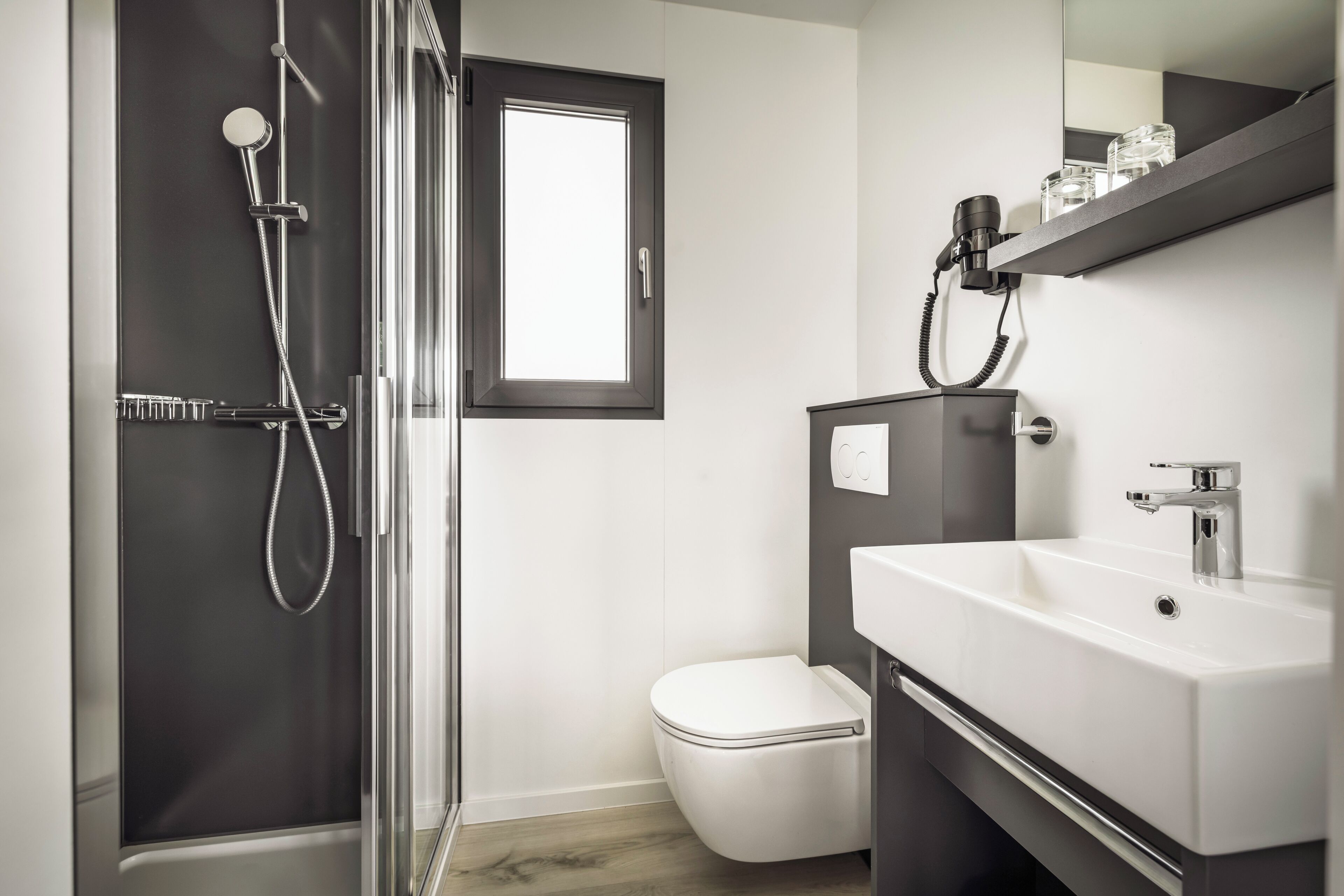 A modern bathroom with a glass shower enclosure, a white toilet, and a vanity with a mirror and shelf.