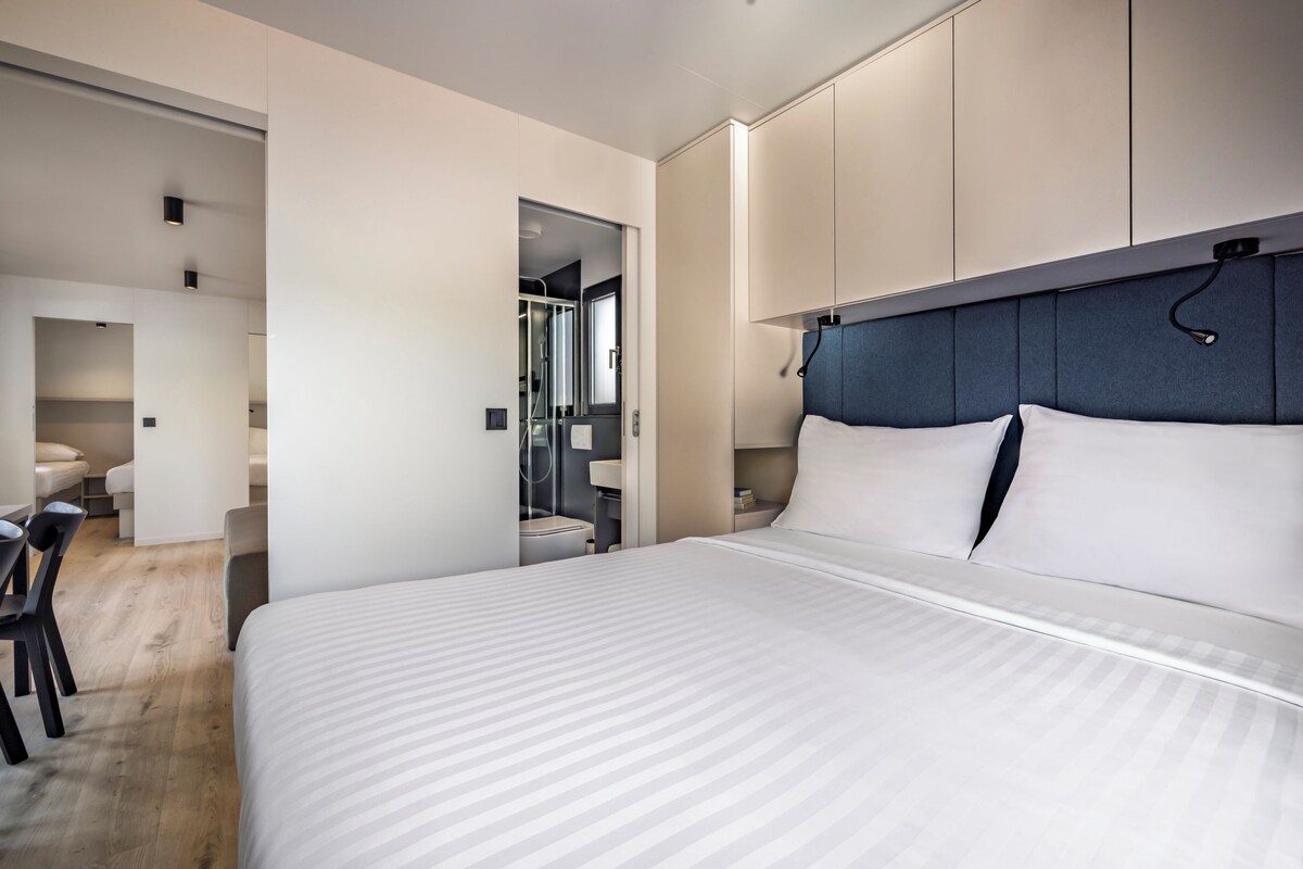 A modern hotel room with a large bed, a desk, and a bathroom visible through an open door.