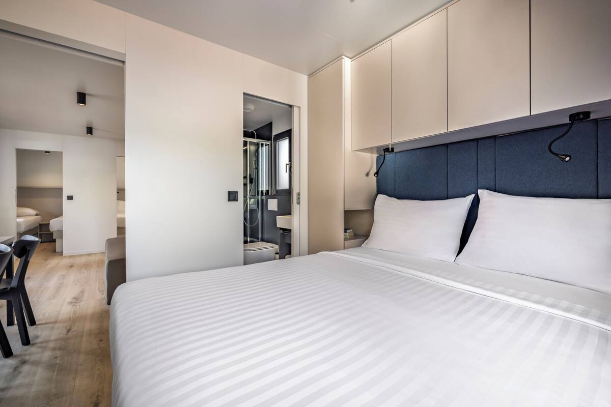 Une chambre d’hôtel moderne, dotée d’un grand lit, d’un bureau et d’une salle de bain visible à travers une porte ouverte.
