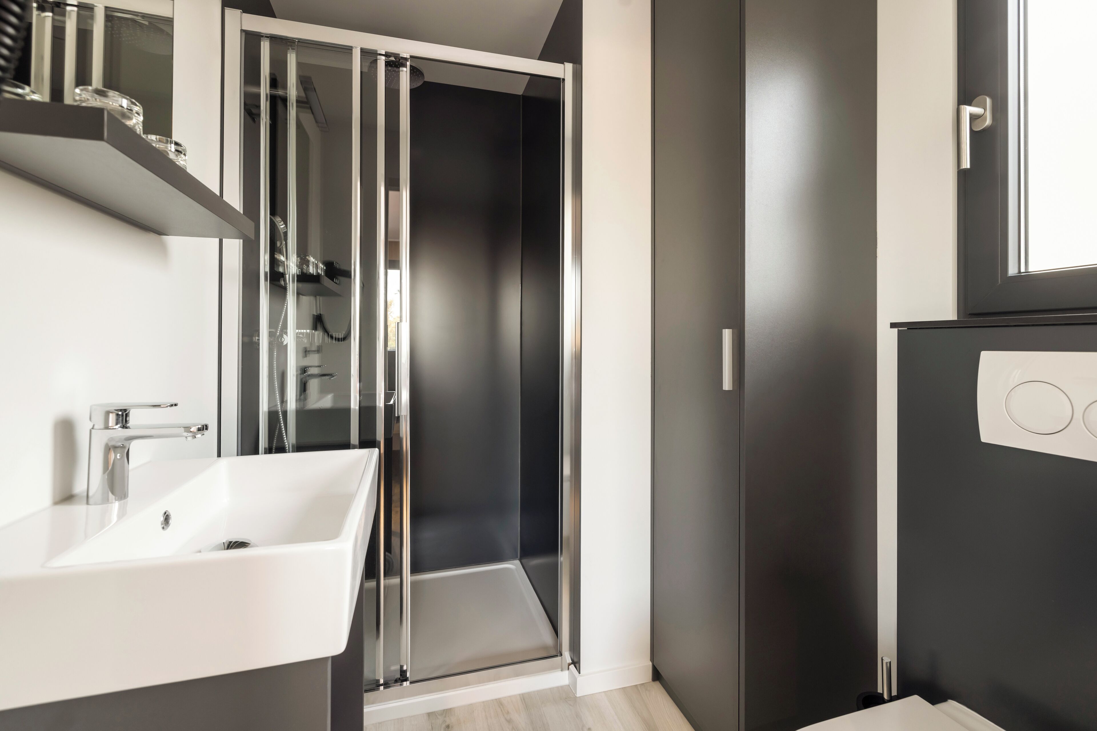 A modern bathroom with a white sink, a glass shower enclosure, and a dark wall.