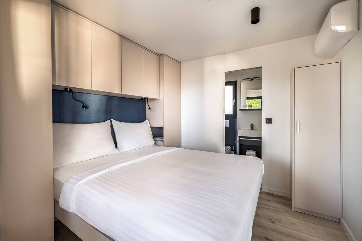 Une chambre à coucher moderne avec un grand lit, une armoire intégrée et une salle de bain visible à travers une porte ouverte.