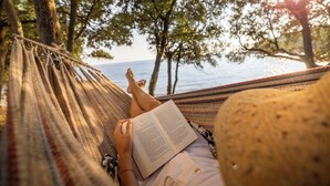 A hammock with a book, set against a backdrop of trees and a body of water.