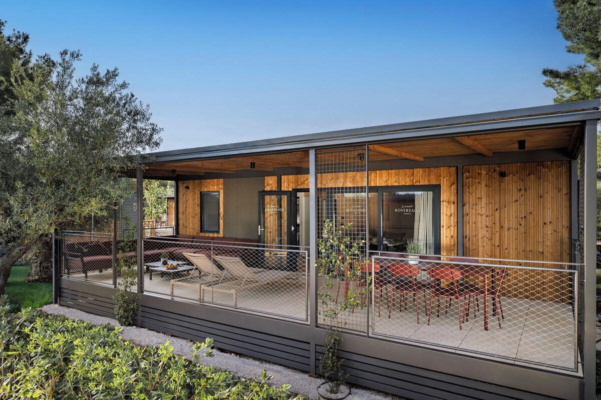 Een modern huis met een overdekt terras, houten gevel en een omheind zitgedeelte buiten.