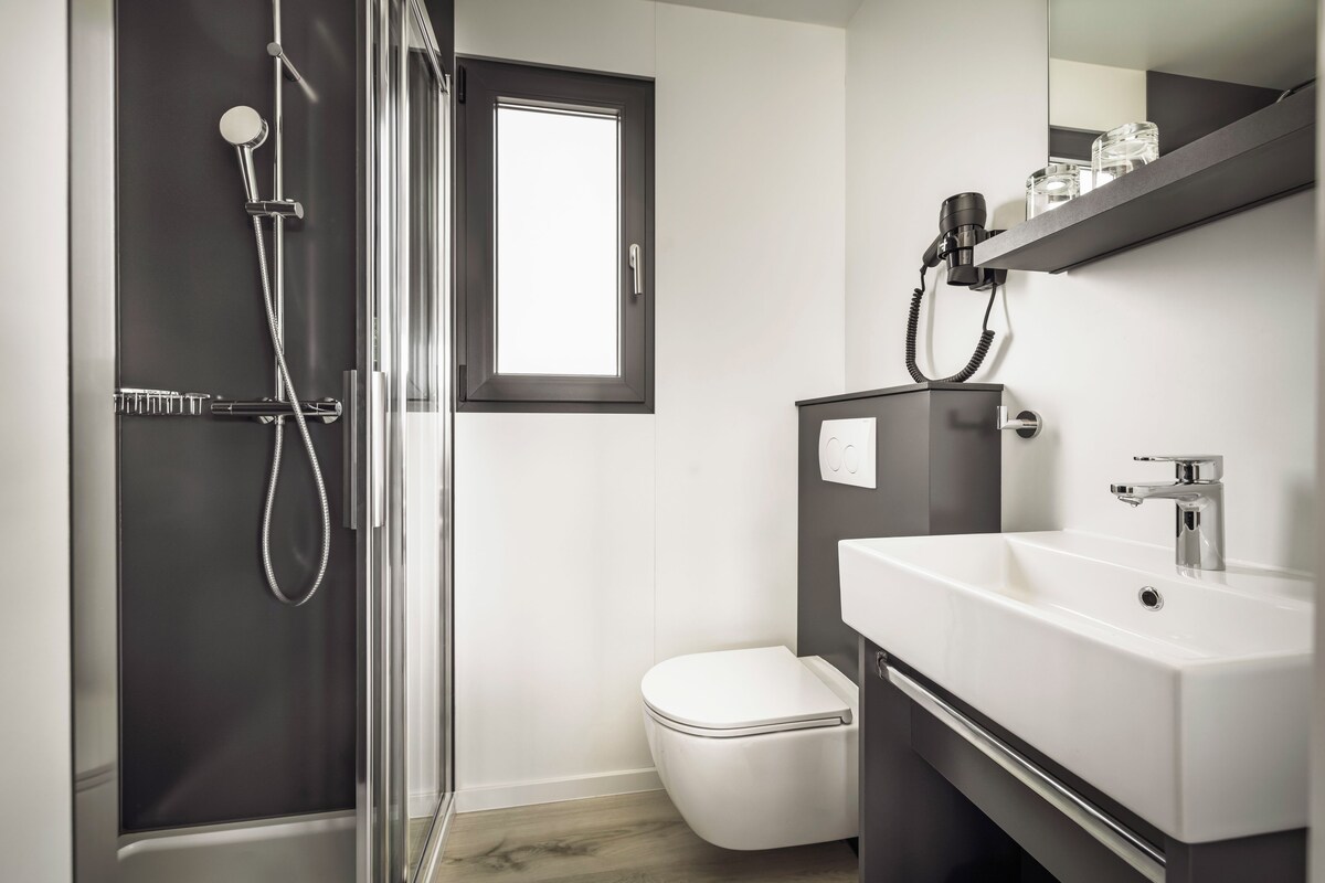 Ein modernes Badezimmer mit Duschkabine aus Glas, Toilette in Weiß und Waschtisch mit Spiegel und Ablagefläche.