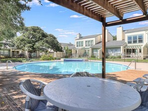 A swimming pool with a wooden deck, surrounded by houses, under a pergola.