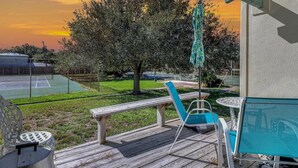 A wooden deck with outdoor furniture, a tennis court, and a tree in the background. - Bayfront Shores RRYC47 (Rockport)