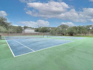 An outdoor tennis court with a net, surrounded by trees and a fence.