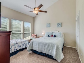 A bedroom with a bed, two bedside tables, a ceiling fan, and a window with blinds.