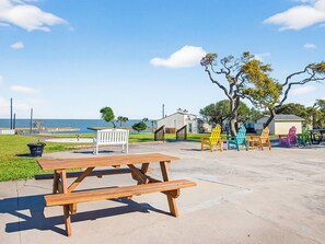 Ein Picknicktisch und bunte Adirondack-Stühle in einer sonnigen Außenanlage mit Blick auf das Meer.