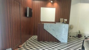 A reception area with a marble counter, wooden panel walls, a tiled floor, and a wall-mounted TV.