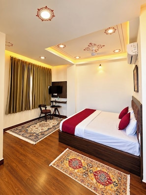A hotel room with a bed, a desk, a chair, a television, and a ceiling with decorative lights. - KALAKAR HAVELI - Udaipur (Udaipur)