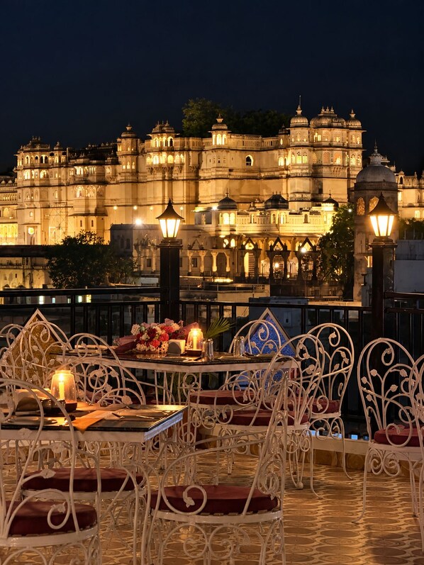 A dining area with ornate metal chairs and tables, set against a backdrop of illuminated historic architecture. - KALAKAR HAVELI - Udaipur (Udaipur)