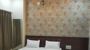 A hotel room with a large bed, a headboard, a nightstand, a ceiling fan, and floral-patterned wallpaper.
