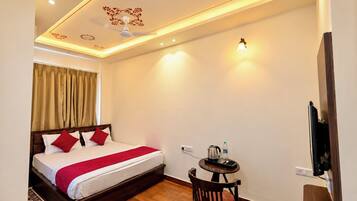 Habitación de hotel con una cama, una mesita con hervidor, una silla y un televisor montado en la pared.