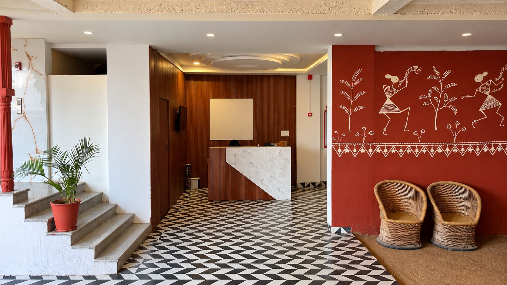 Un hall d’hôtel avec un comptoir d’enregistrement, un escalier orné d’une plante en pot et un sol à motifs.