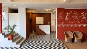 A hotel lobby with a check-in counter, a staircase with a potted plant, and a patterned floor. - KALAKAR HAVELI - Udaipur (Udaipur)
