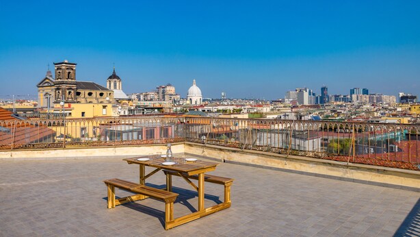 A rooftop terrace with a wooden table and benches, overlooking a cityscape with historic buildings and a modern skyline. - Terrazzo Panoramico su Napoli by Wonderful Italy (Napoli)
