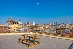 A rooftop terrace with a wooden table and benches, overlooking a cityscape with historic buildings and a modern skyline. - Terrazzo Panoramico su Napoli by Wonderful Italy (Napoli)
