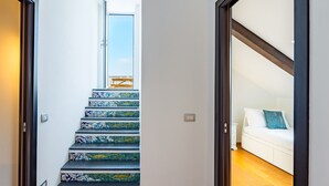 A staircase with patterned steps leading to a door, a white sofa with a blue pillow, and a wooden floor. - Terrazzo Panoramico su Napoli by Wonderful Italy (Napoli)