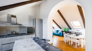 A modern kitchen with a marble countertop, stainless steel appliances, and a dining area with white furniture. - Terrazzo Panoramico su Napoli by Wonderful Italy (Napoli)