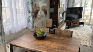 Un comedor con mesa de madera y banco, una lámpara colgante tejida y vistas al exterior a través de amplios ventanales.