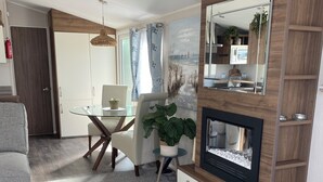 Una sala de estar moderna con una mesa de comedor de vidrio, un sofá cómodo, una chimenea y un aparador de madera con espejo.