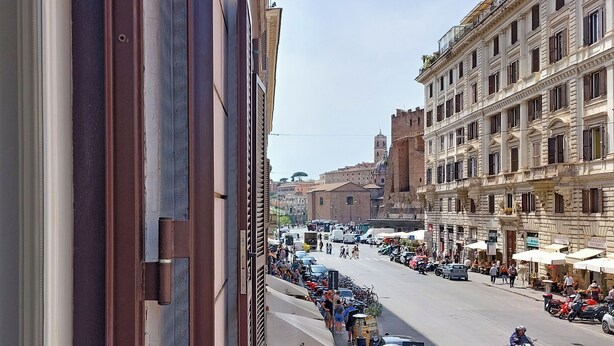 Une vue de rue avec une rangée de voitures garées et un immeuble doté d’un balcon.