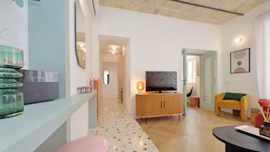 Un salon moderne avec un téléviseur, un meuble en bois et un tabouret rose.
