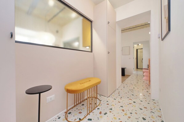 A hallway with a small round table and a bench, a tiled floor, and a door leading to a bathroom. - Luxury apartment near Fori Imperiali (Rome)