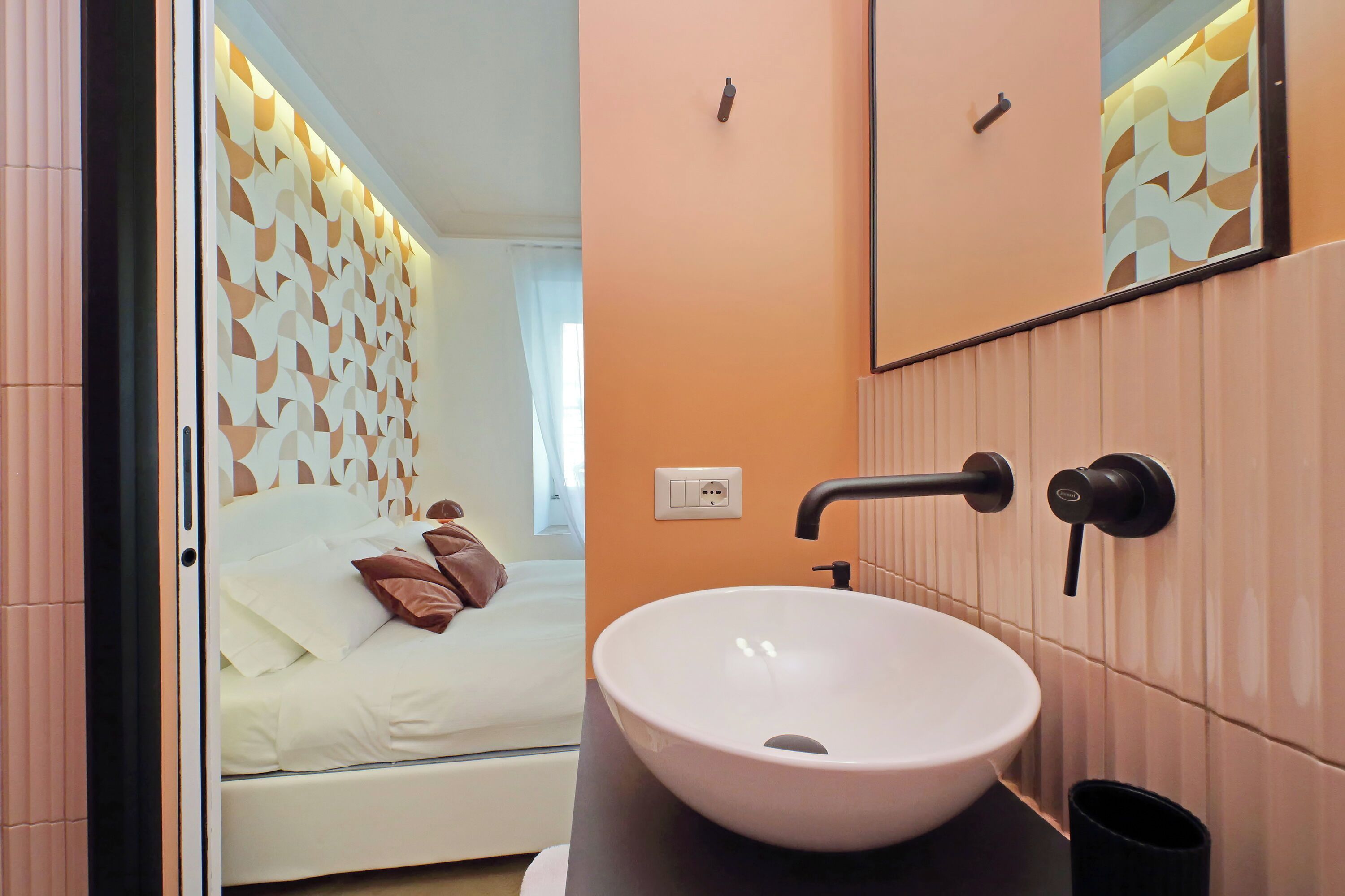 Un baño moderno con un lavabo grande de color blanco, un espejo y una cama con ropa de cama blanca y almohadas marrones.