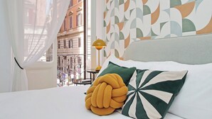 Une chambre d’hôtel avec un lit, une fenêtre avec des rideaux, un mur à motifs et une vue sur les bâtiments environnants.