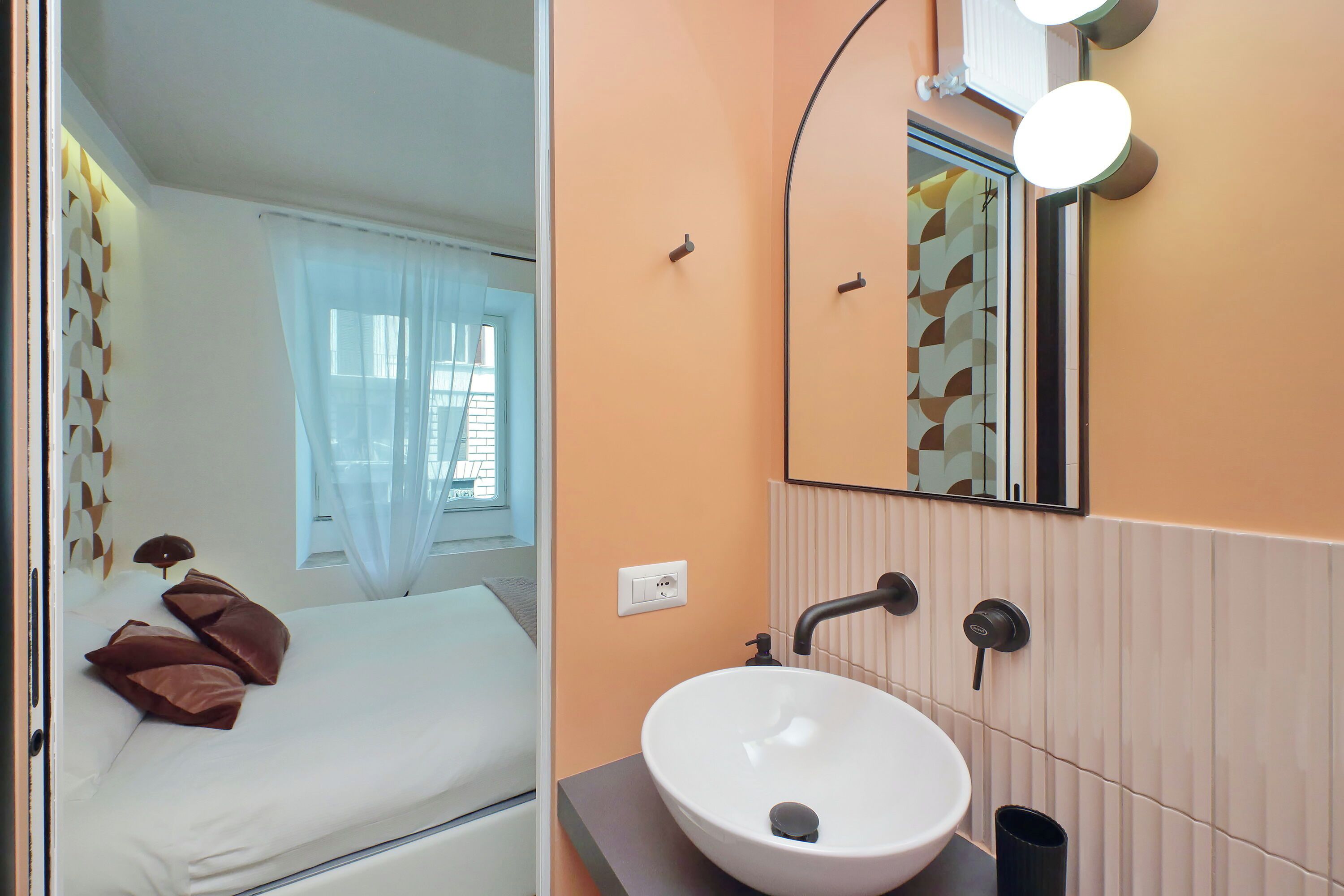 A modern bedroom with a bed, a white sink, and a mirror with lights.