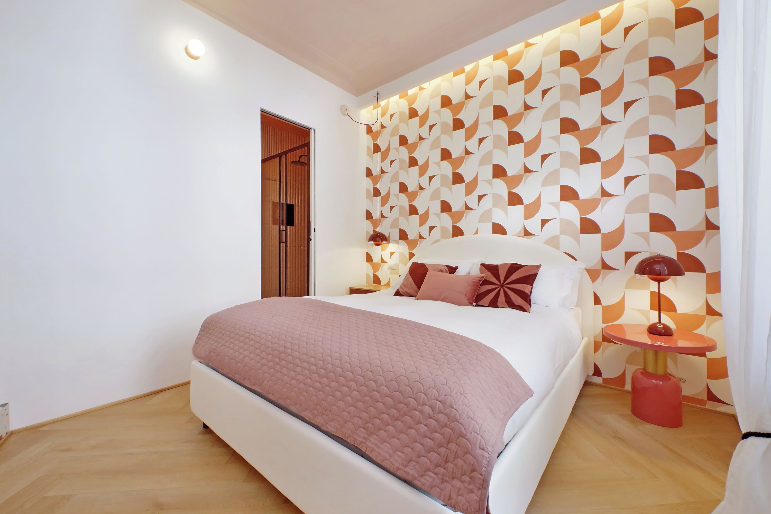 A modern bedroom with a large bed, a patterned wall, and a bedside table with a lamp.