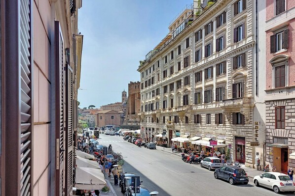A street view with historic buildings, outdoor seating, and parked cars.