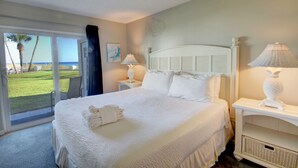A hotel room with a large bed, a nightstand with lamps, a view of the ocean through a sliding door, and a painting on the wall.