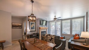A dining area with a wooden table and chairs, a fireplace, a television, and a sofa with cushions. - Premium Unit 4285 Fraser Crossing/founders Pointe 2 Bedroom Condo (Winter Park)