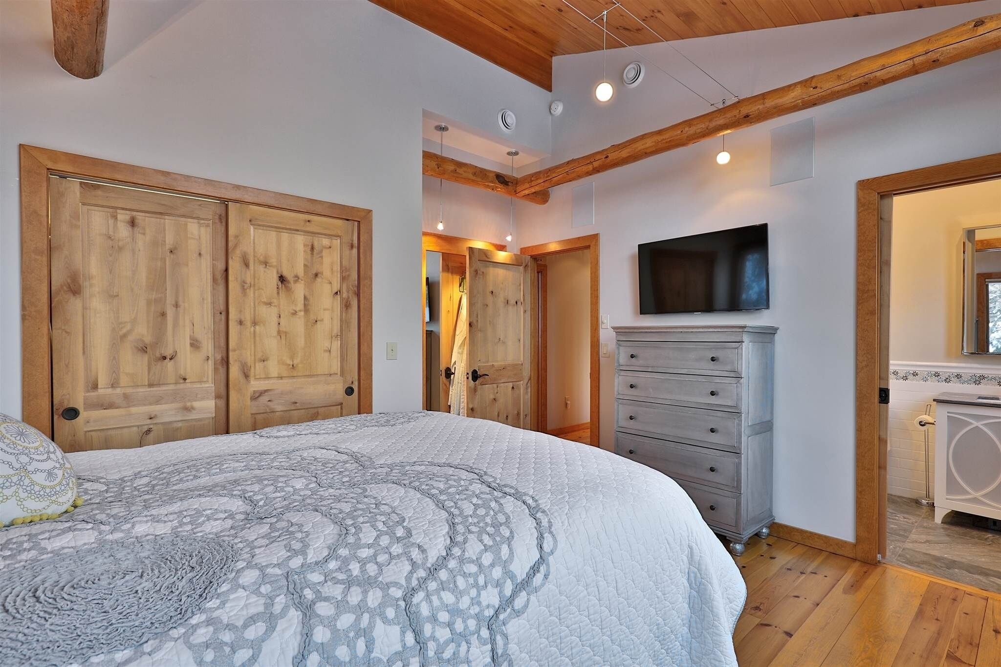 A bedroom with a large bed, wooden wardrobe, a dresser, and a television mounted on the wall.