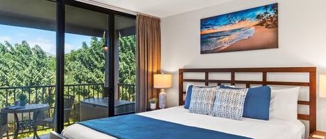 Ein Hotelzimmer mit einem großen Bett, einem Deckenventilator, einem Balkon mit Tisch und Stühlen sowie einem Bild mit einer Strandansicht.