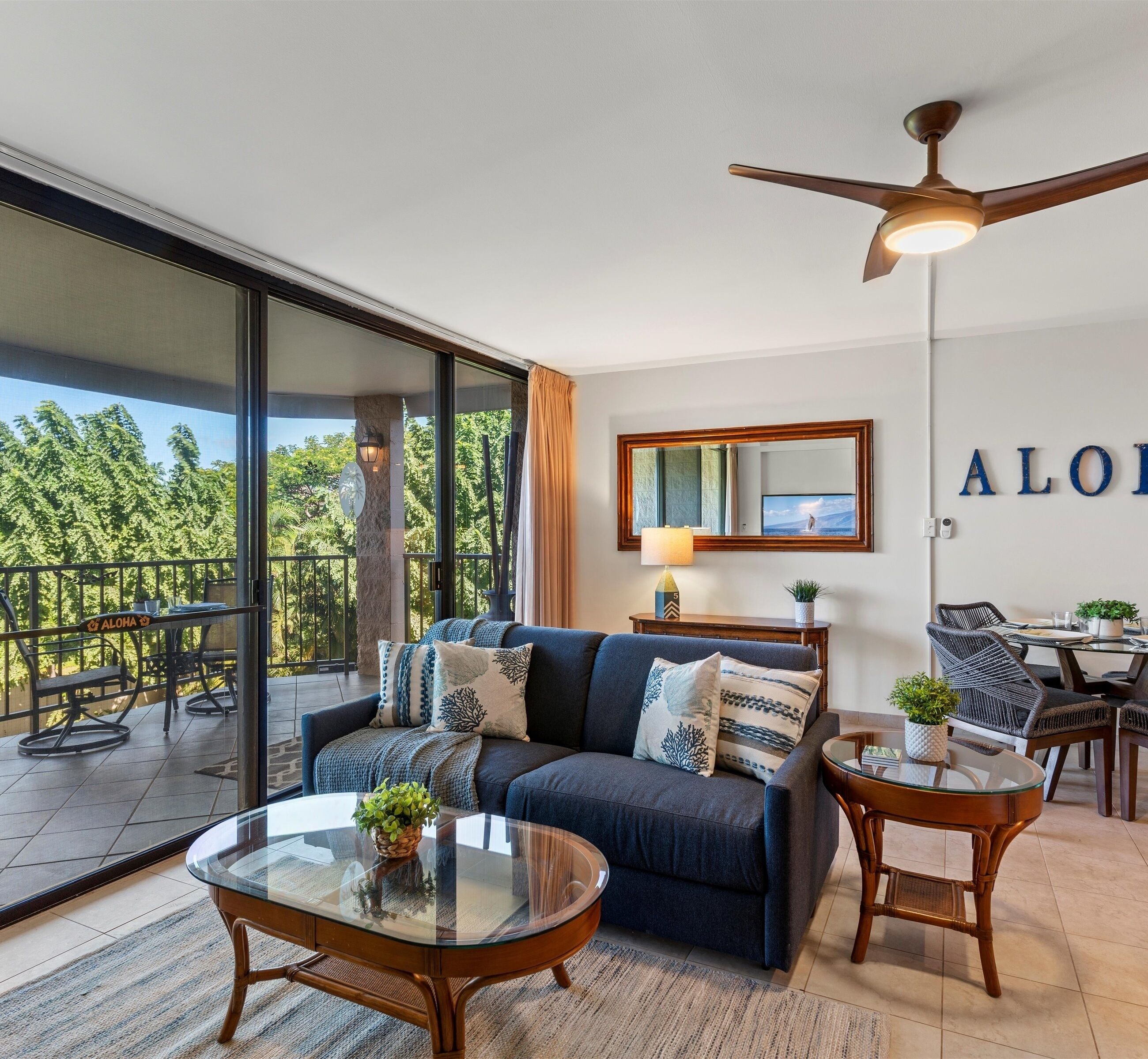 A modern living room with a sofa, coffee table, and chairs, a balcony with outdoor furniture, and a ceiling fan.
