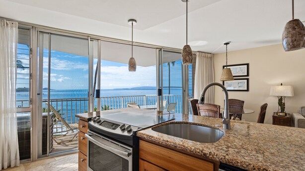 Una cocina con una isla grande, vistas al océano y un comedor con sillas.