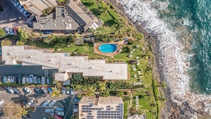 An aerial view of a coastal hotel with a swimming pool, parking, and a view of the ocean. - Kamaole Nalu, #405 2 Bedroom Condo (Kihei)