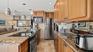 A modern kitchen with granite countertops, stainless steel appliances, wooden cabinets, and a built-in oven. - Kamaole Nalu, #405 2 Bedroom Condo (Kihei)