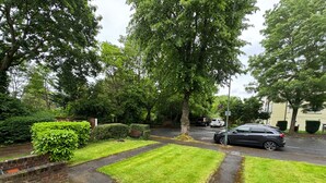A residential street with a paved path, lush greenery, and parked cars. - Lovely 2 Bedrooms Flat in South Sutton (Sutton)