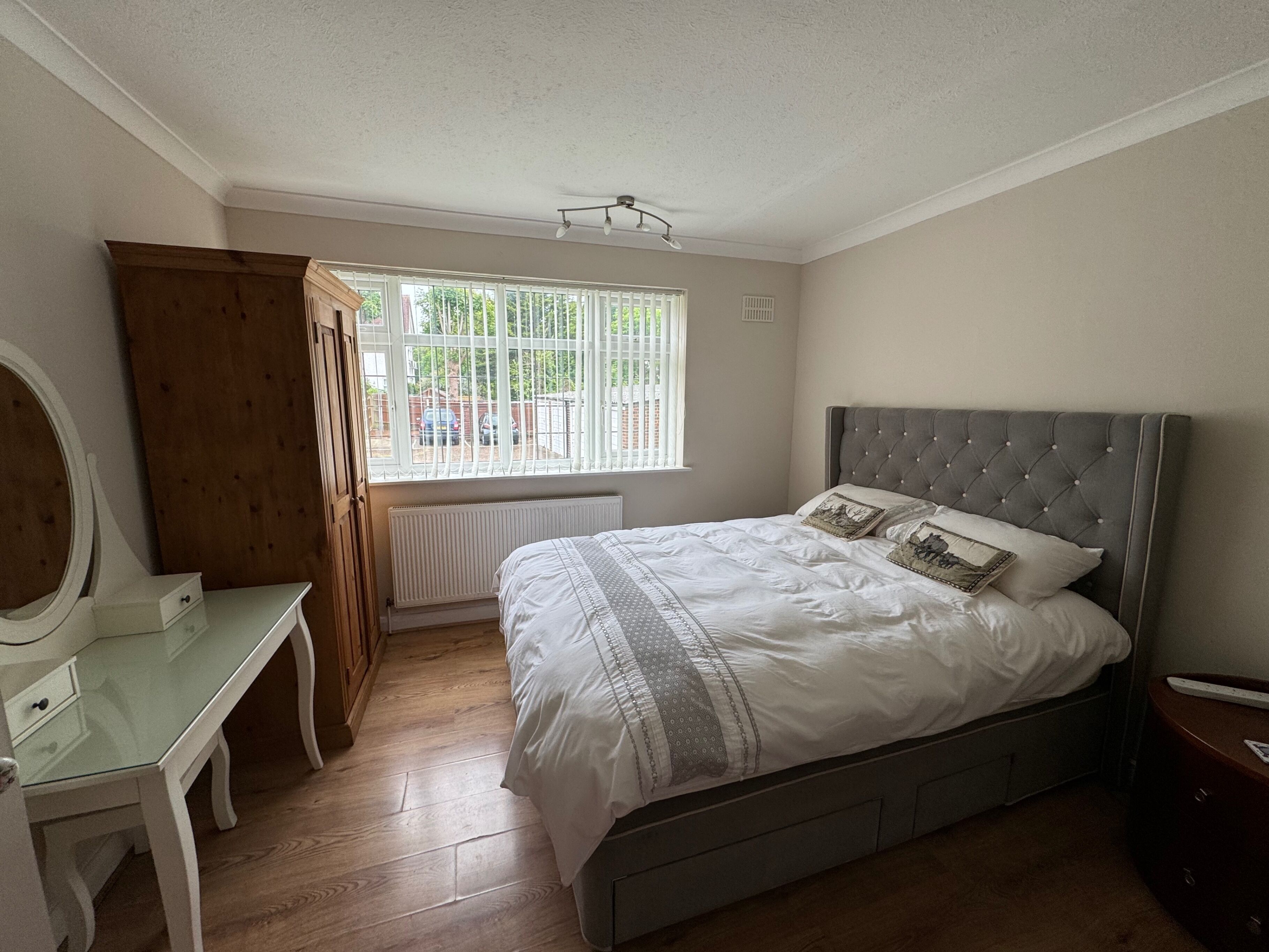 A bedroom with a bed, a dresser, a mirror, and a window with blinds.