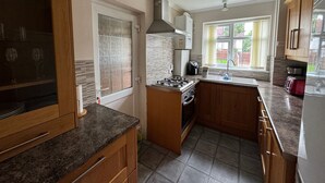 A kitchen with wooden cabinets, a gas stove, a built-in oven, a window with a view of the outside, and a ceiling fan. - Lovely 2 Bedrooms Flat in South Sutton (Sutton)
