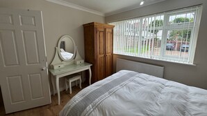 A bedroom with a bed, a dresser, a mirror, a window with blinds, and a radiator. - Lovely 2 Bedrooms Flat in South Sutton (Sutton)