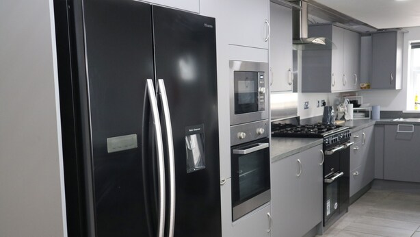 A modern kitchen with stainless steel appliances, grey cabinets, and a tiled floor.
