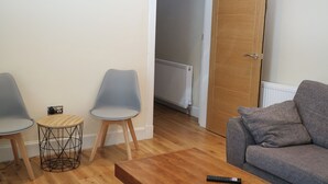 A living room with a grey sofa, two grey chairs, a wooden coffee table, and a small round side table with a wireframe base.
