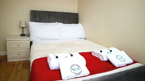 A neatly made bed with white linens, a red blanket, and two towels with a logo on them.